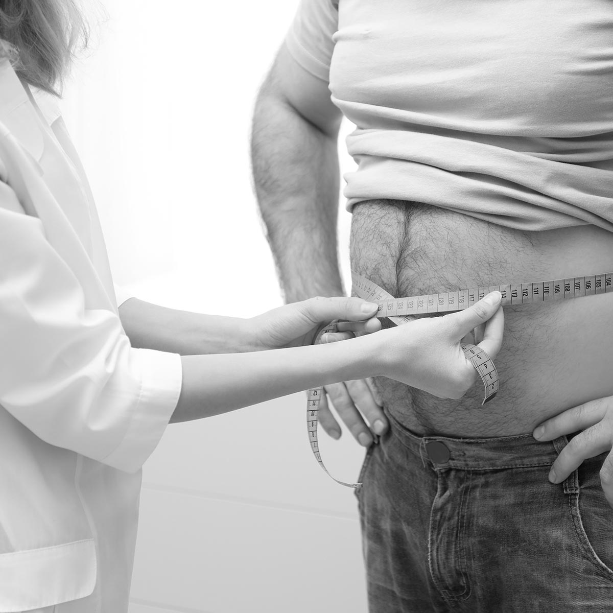 Doctor measuring overweight man's waist in hospital, closeup
